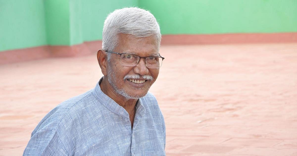 Poomani, a grey-haired man in glasses and a blue shirt, smiling outdoors