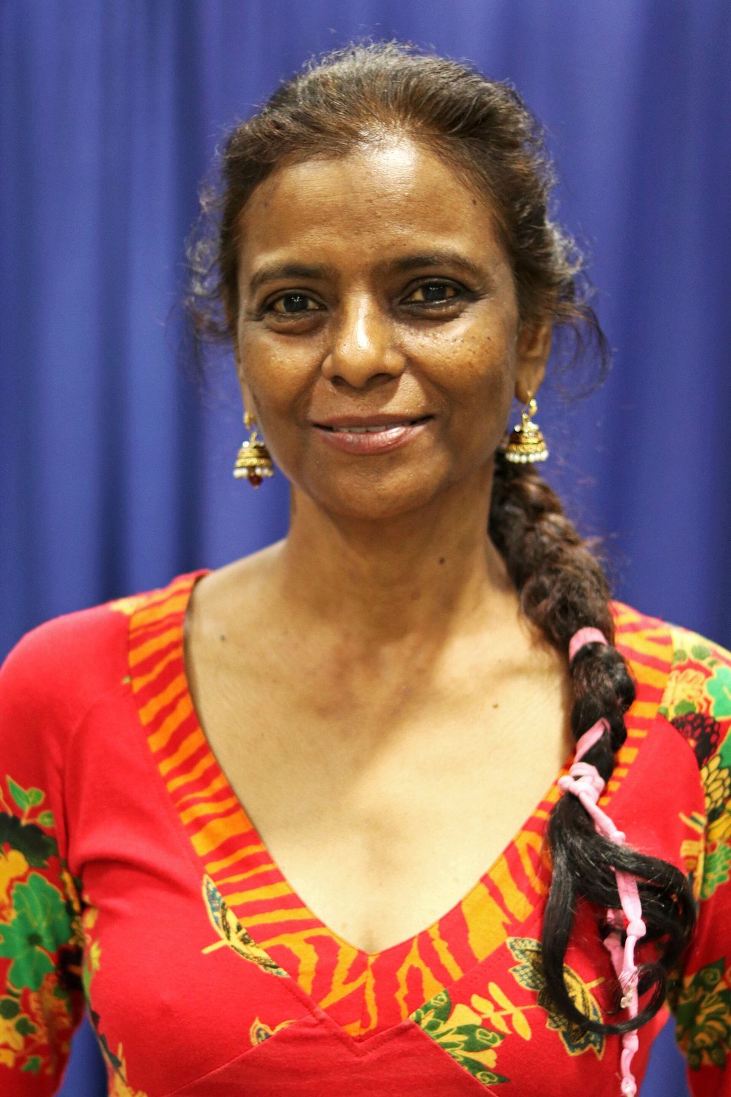 Sujatha Gidla smiling in front of a blue curtain, wearing a red floral top, at the 2018 National Book Festival in Washington