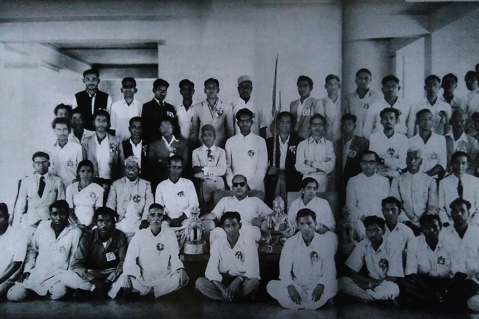 Black-and-white group photograph of adults seated and standing in rows, with B.R. Ambedkar seated near a small Buddha statue
