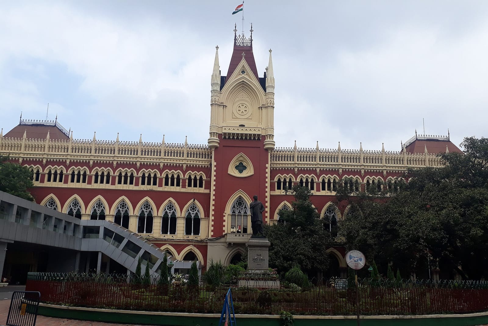 The red and cream Gothic facade and central tower of the Calcutta High Court in Kolkata, behind a garden railing