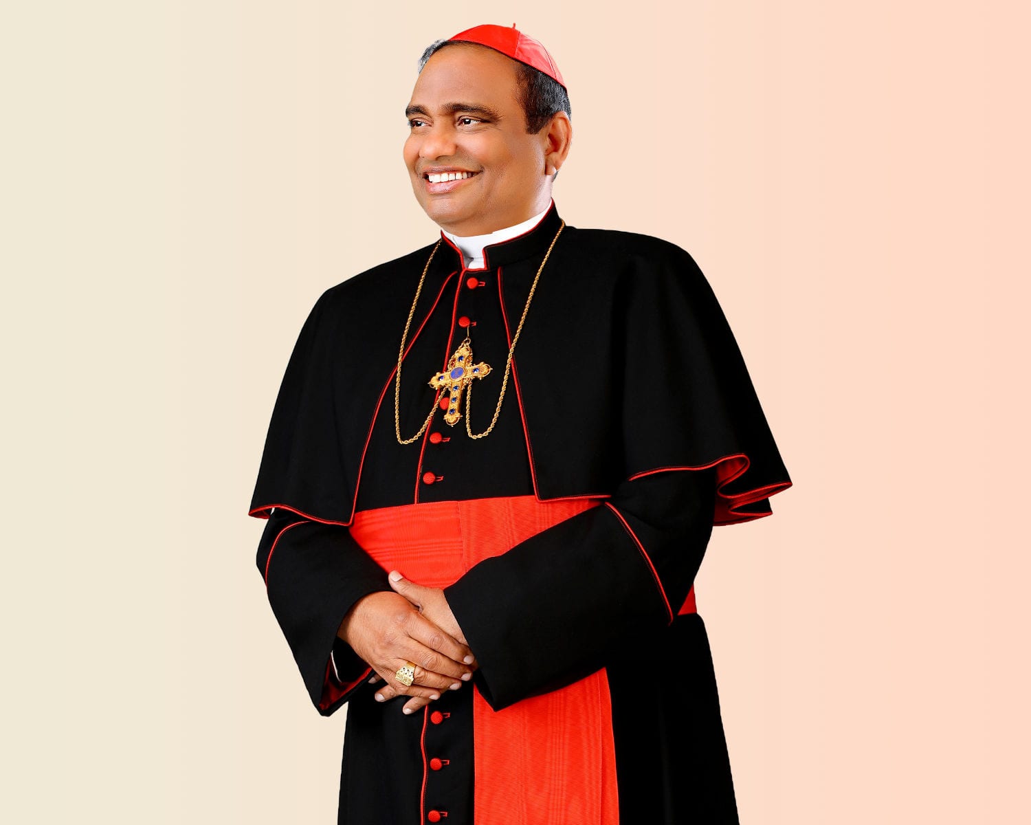 Cardinal Anthony Poola, smiling, in a black cassock with red trim and a red skullcap, hands folded