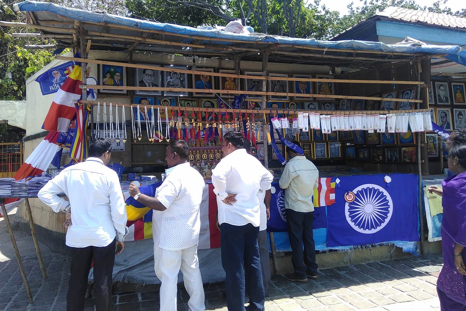 Shoppers at a stall hung with framed portraits of B.R. Ambedkar and the Buddha, blue Ambedkarite flags and Buddhist flags