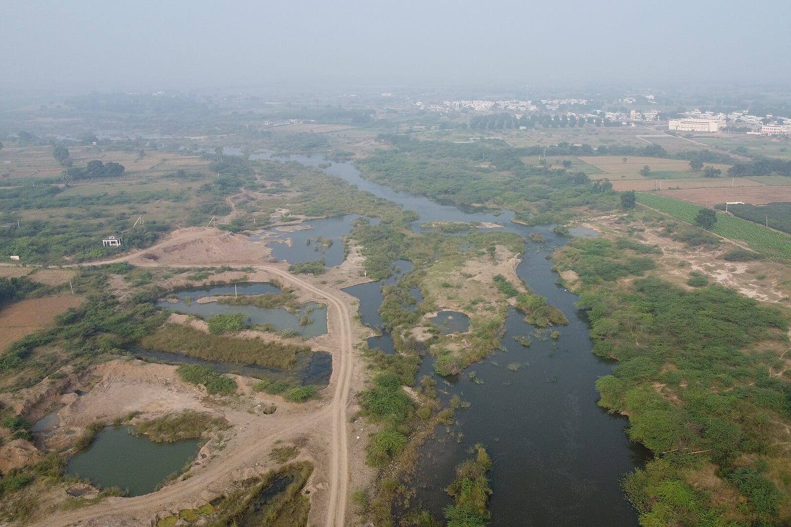 An aerial view of the Gundlakamma river winding through scrub, fields and sand pits, with a town's buildings in the haze beyond