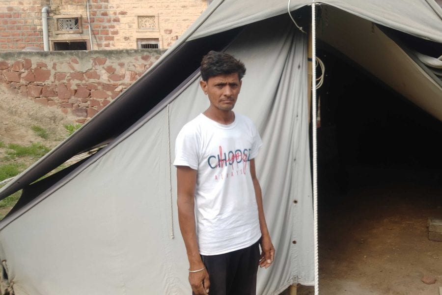 A young man in a white T-shirt stands beside a grey police tent outside a house in Dangawas, Rajasthan