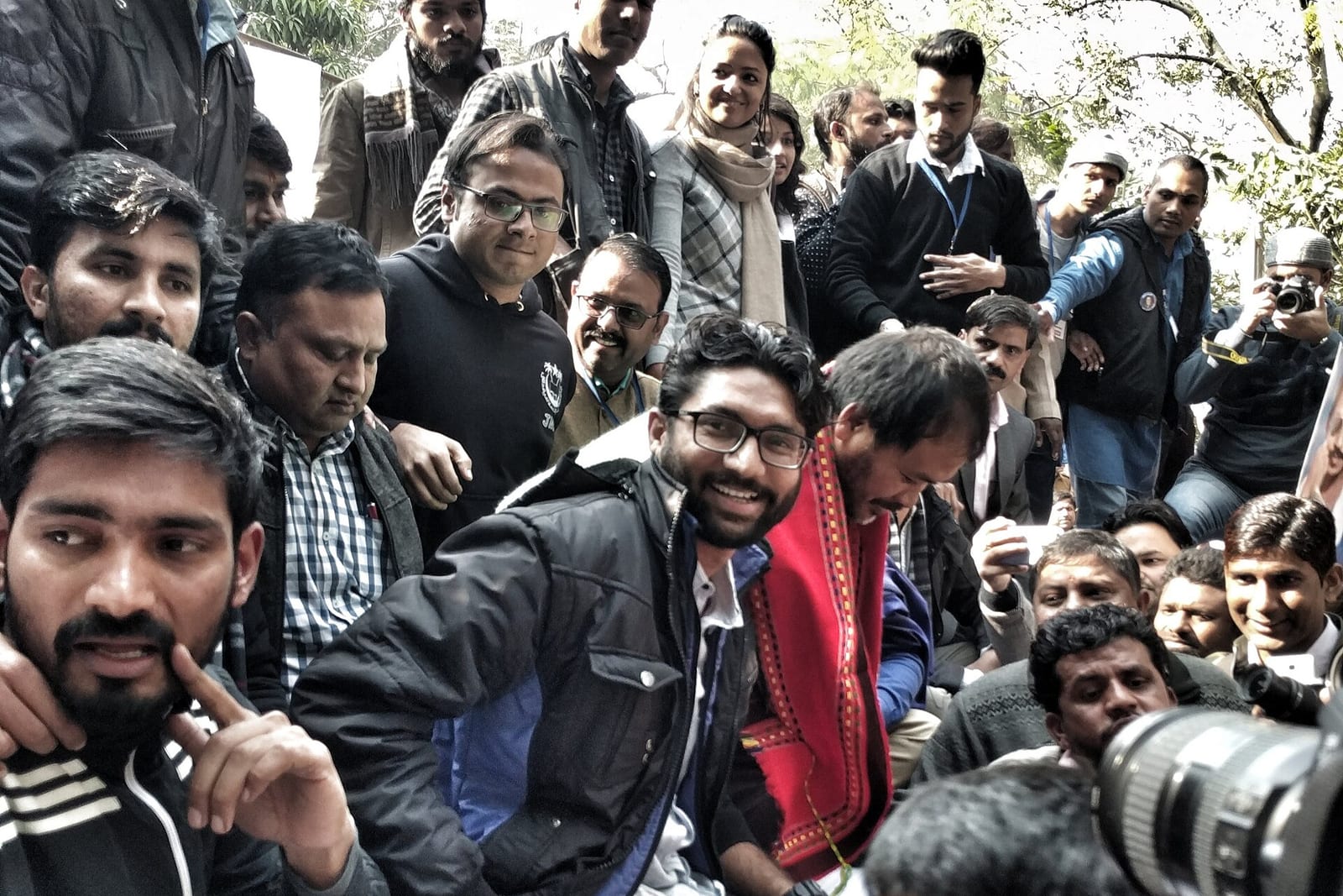 Jignesh Mevani, in glasses and a dark jacket, seated among supporters and press photographers at a rally in New Delhi