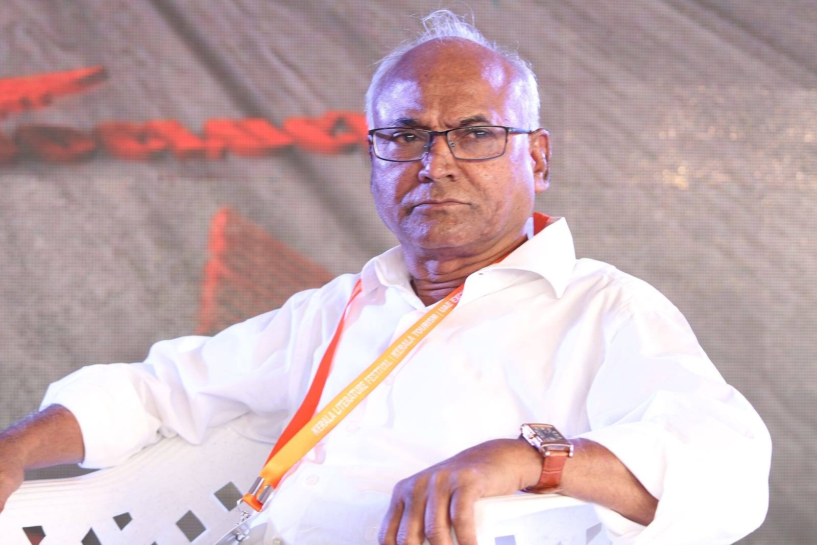 Kancha Ilaiah Shepherd, in a white shirt and a festival lanyard, seated on stage at the Kerala Literature Festival