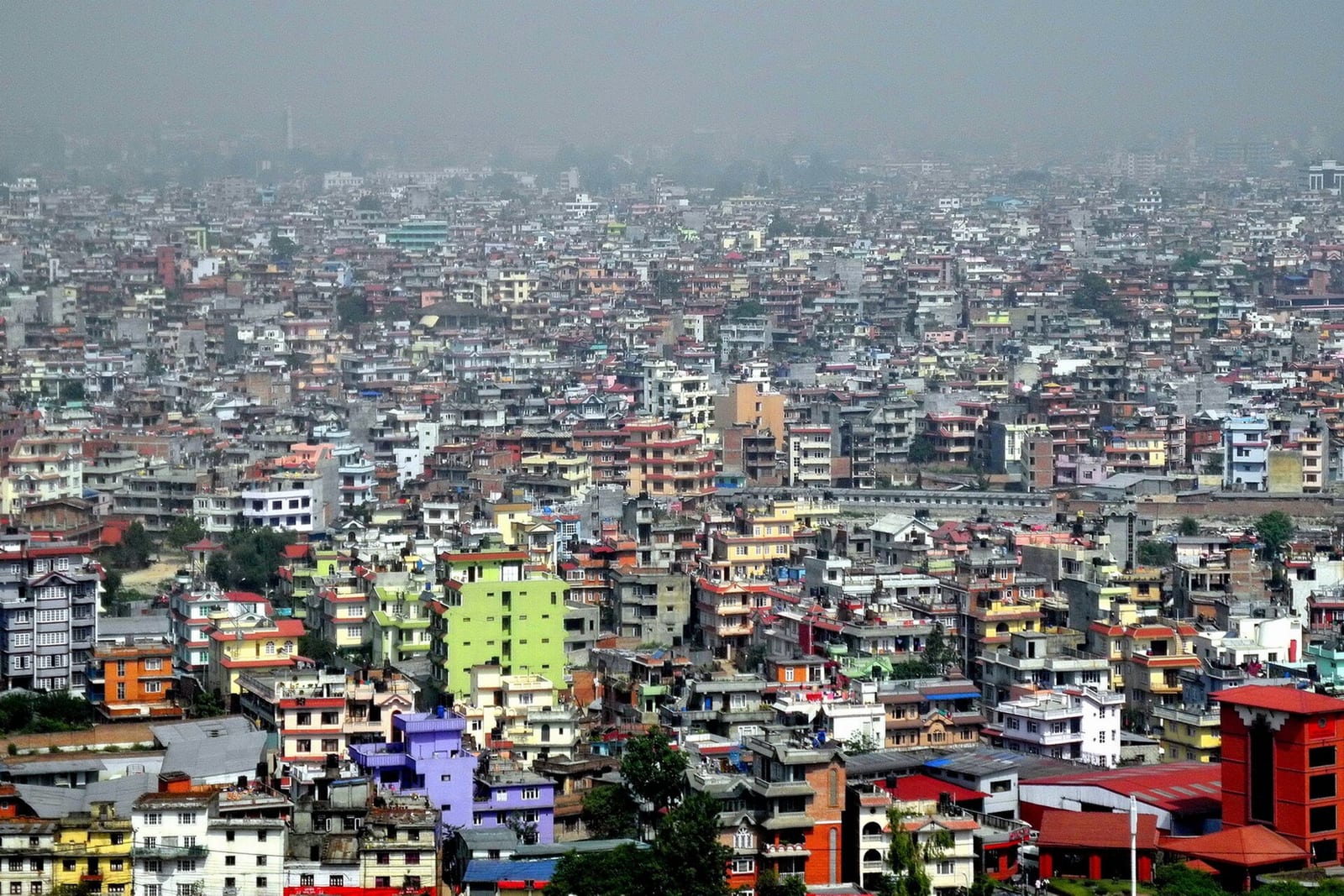 Densely packed, multi-coloured houses and apartment blocks stretching across Kathmandu under a hazy sky