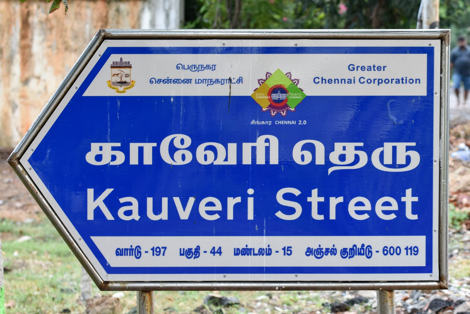 A blue arrow-shaped Greater Chennai Corporation street sign reading Kauveri Street in Tamil and English, on two posts in Uthandi, Chennai