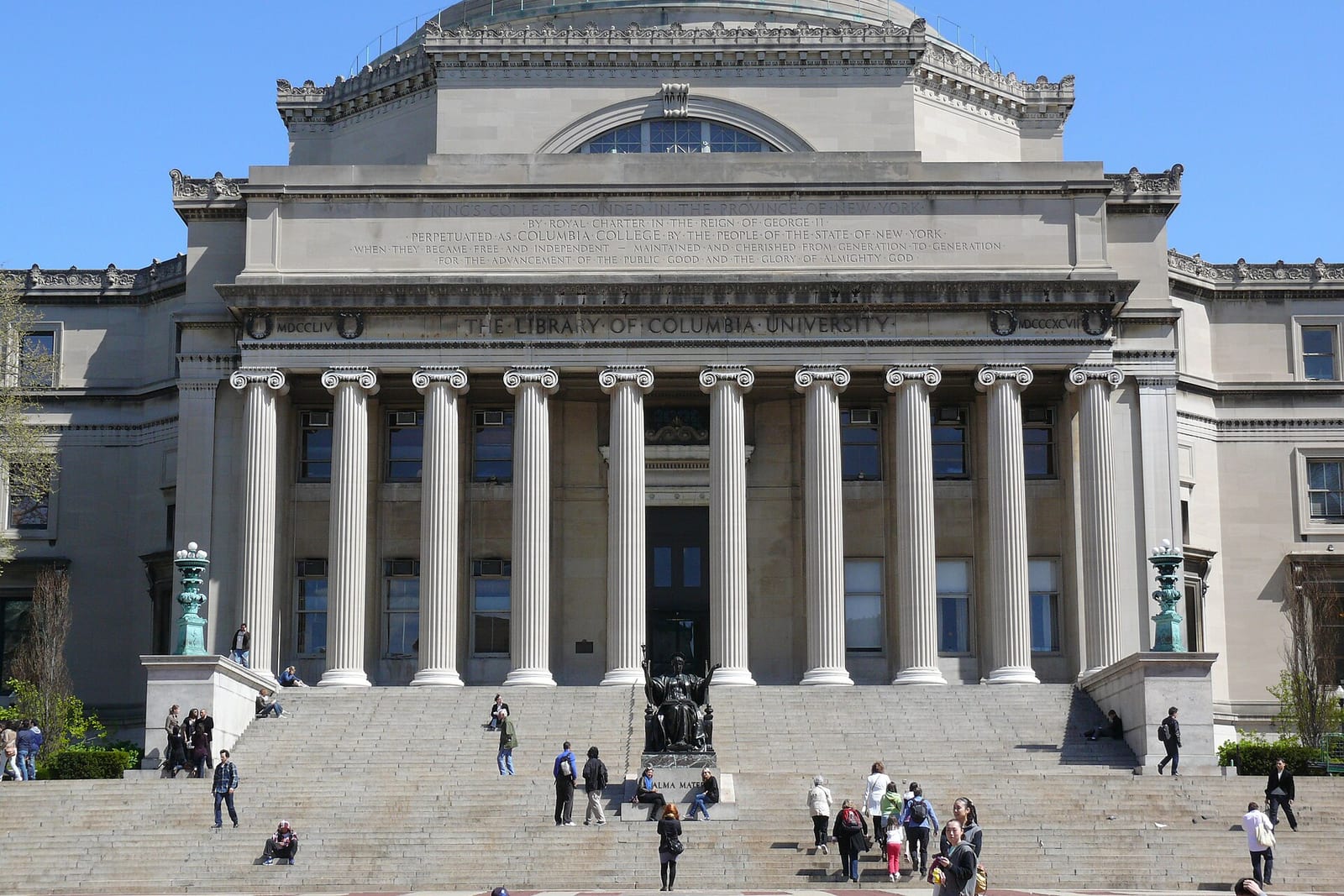 Low Memorial Library at Columbia University, a domed stone building with a row of columns above wide steps and a seated bronze statue, people walking on the steps