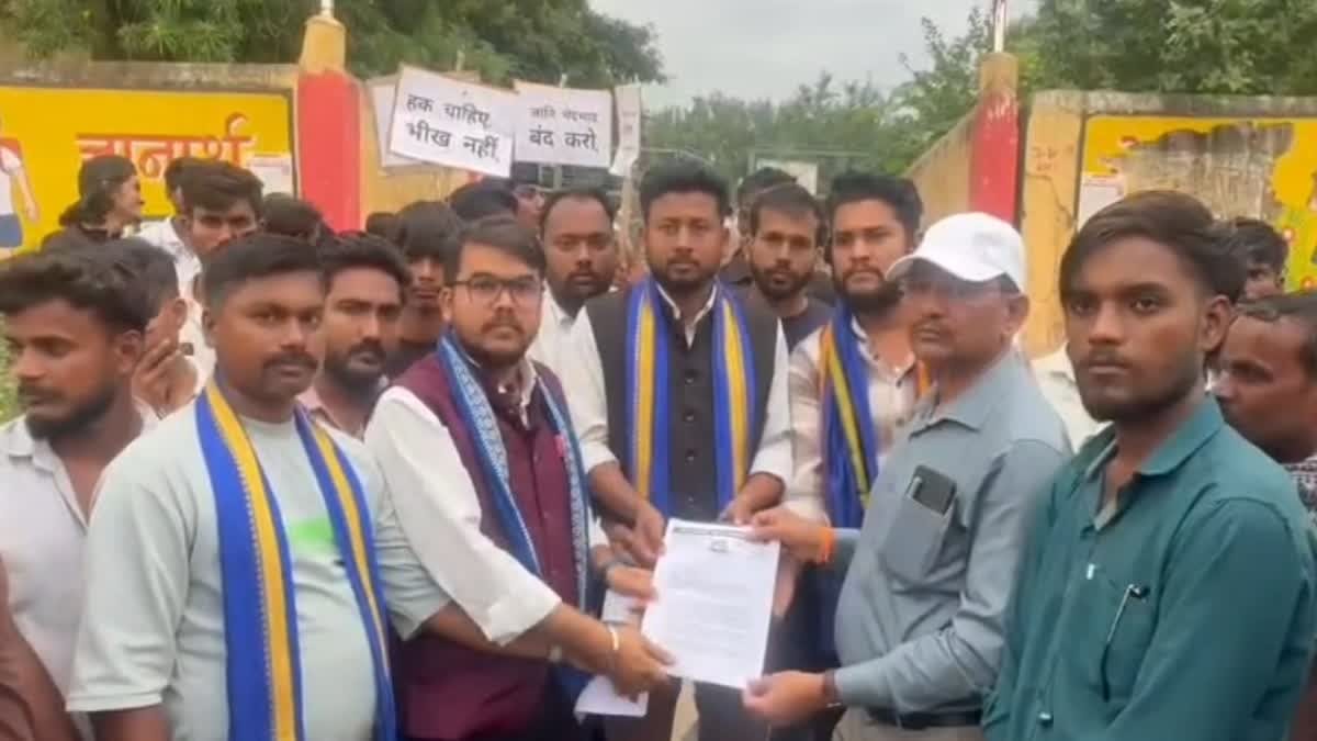 Bhim Army members, several wearing blue and yellow scarves, hand a memorandum to an official outside a school gate; placards behind them read, in Hindi, 'We want rights, not alms' and 'End caste discrimination'
