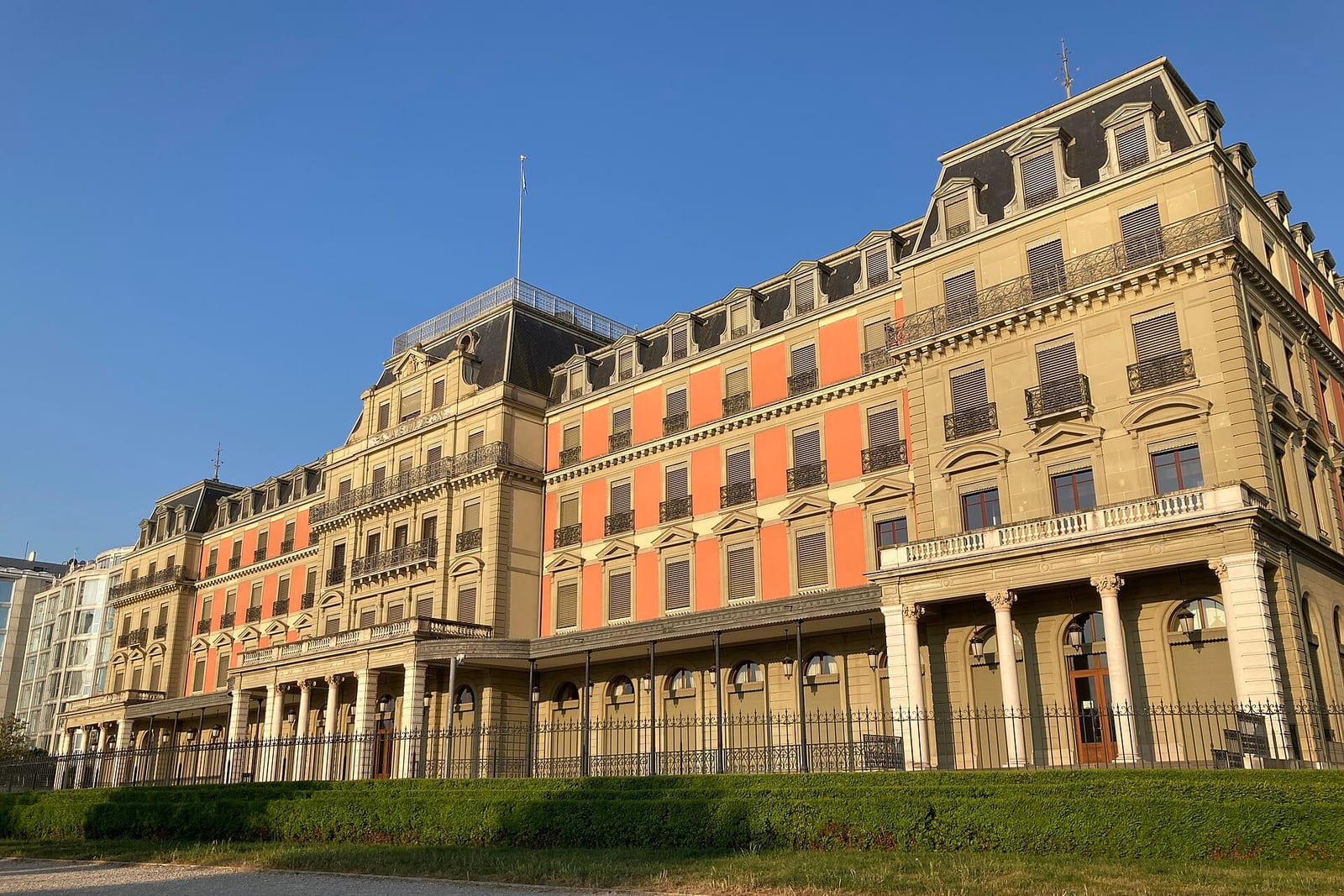A large 19th-century building with pink and stone facades, a mansard roof and a columned porch behind a lawn