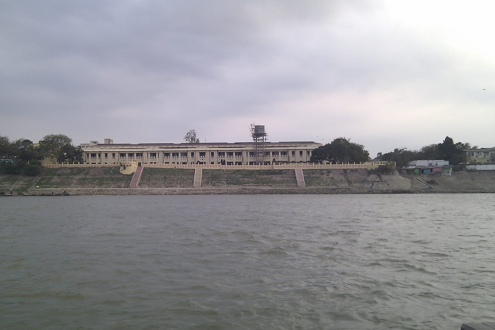A long, low cream-coloured court building on a riverbank, seen across grey water under an overcast sky