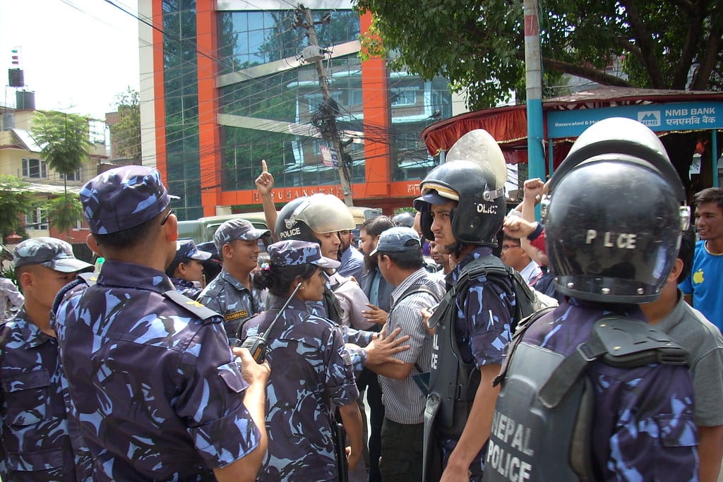 Riot police in helmets marked Nepal Police face Dalit rights protesters with raised fists on a Kathmandu street