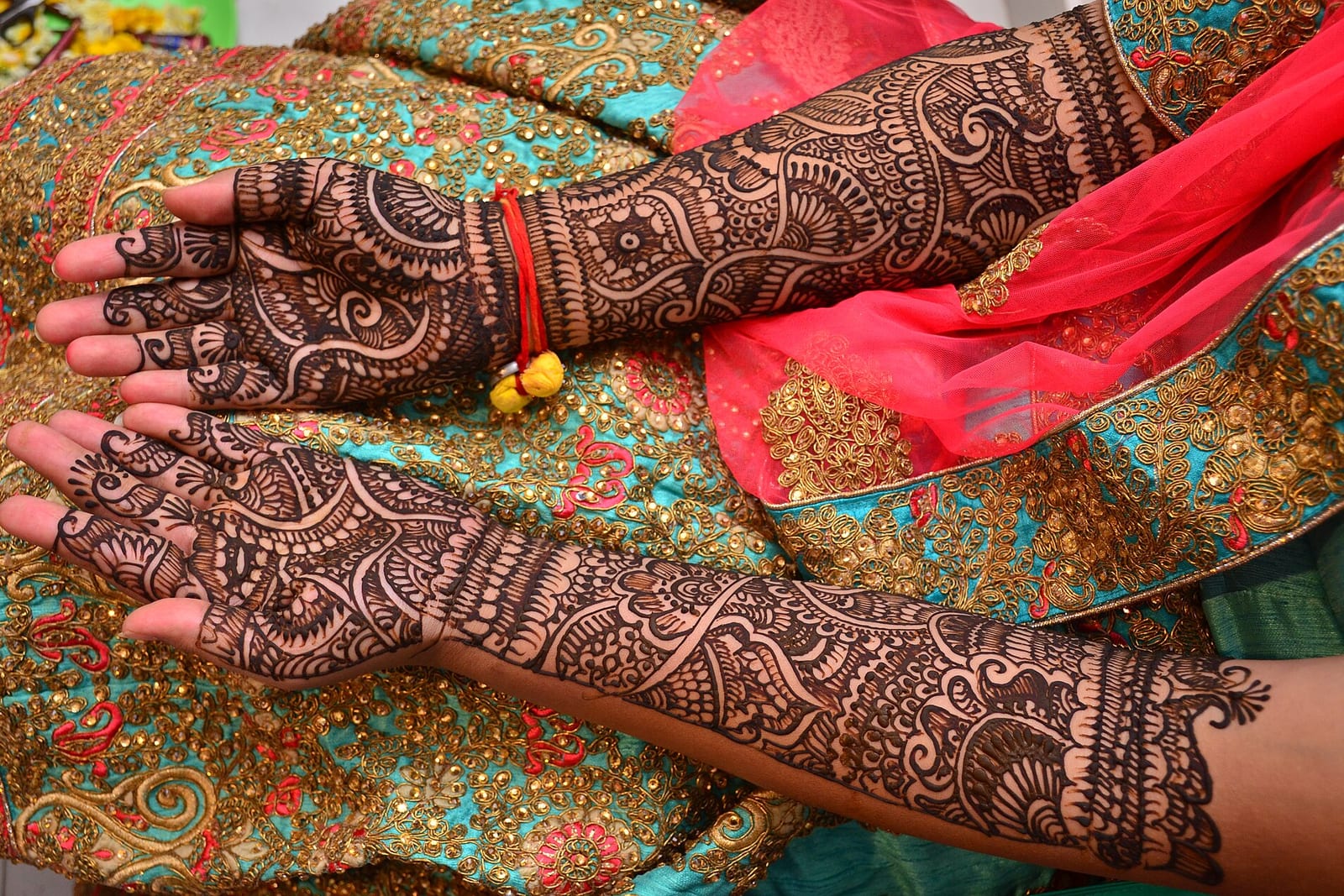 A bride's hands covered in fine mehendi patterns, resting on a brightly embroidered cloth