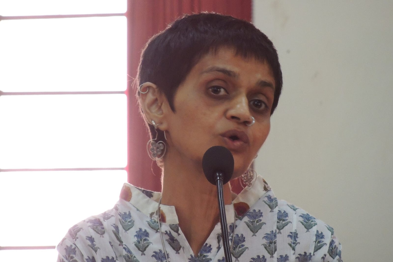 Sharmila Rege speaking into a microphone at a public event