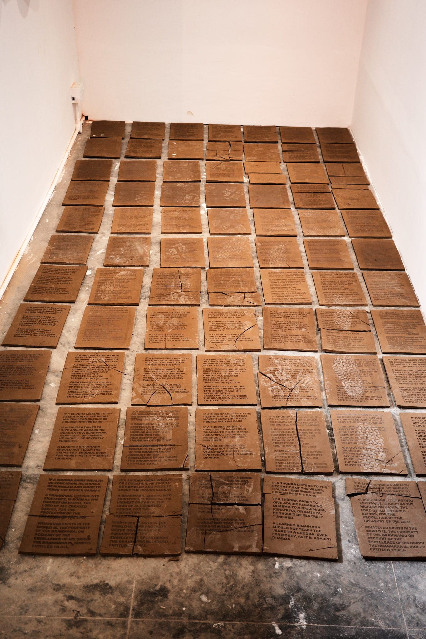 Rows of unfired clay tiles inscribed with text laid across a gallery floor