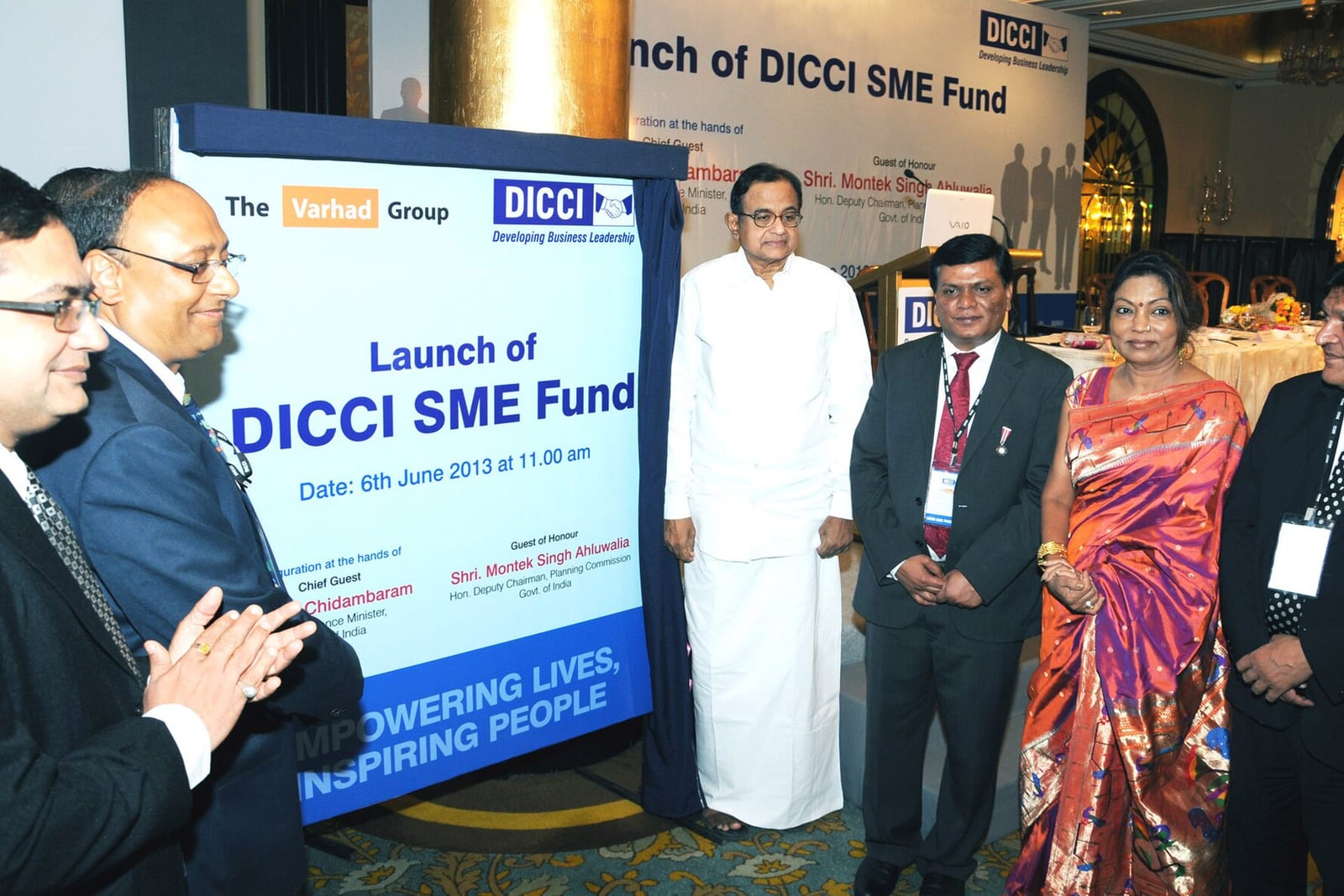 A man in white unveils a DICCI SME Fund banner beside men in suits and a woman in a sari