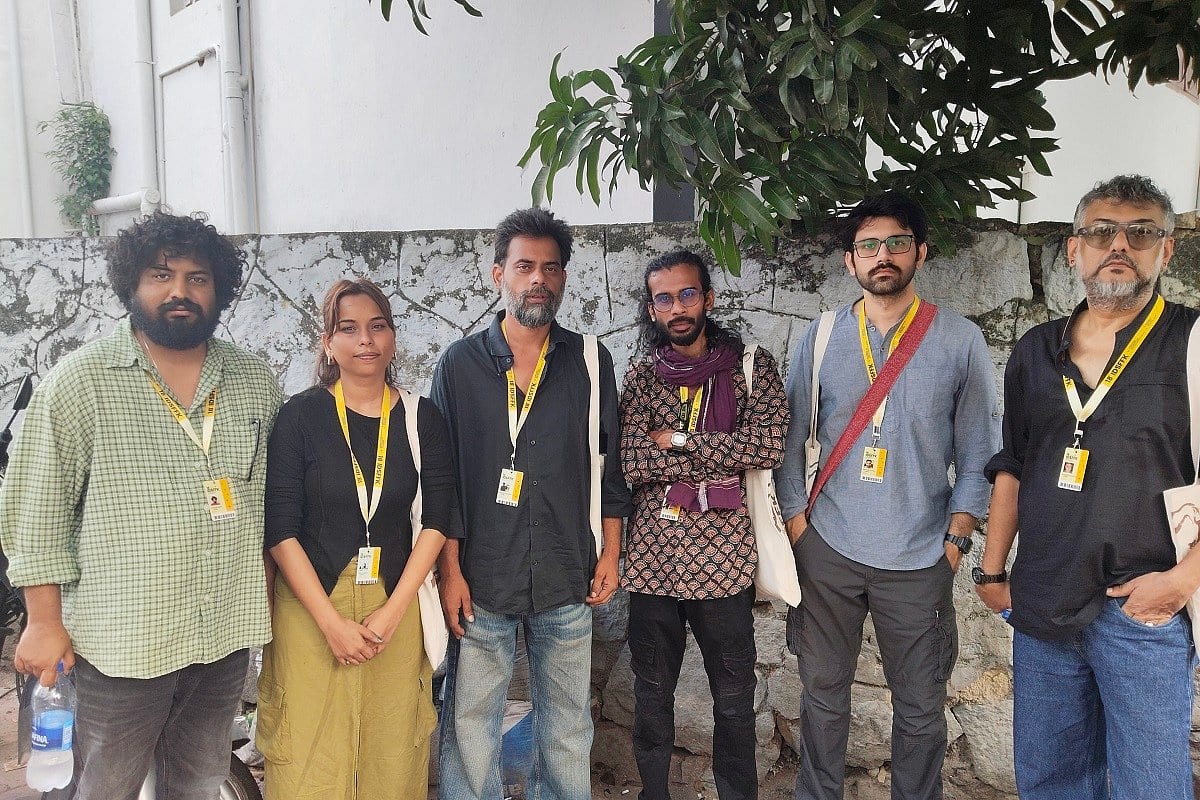 Six filmmakers wearing festival lanyards stand together against a wall at the documentary festival in Thiruvananthapuram