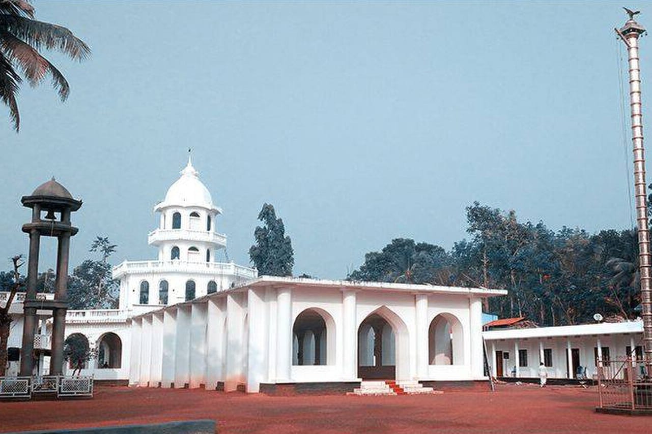 A white domed hall with arched openings and a bell tower in a red-earth compound at Eraviperoor, Kerala